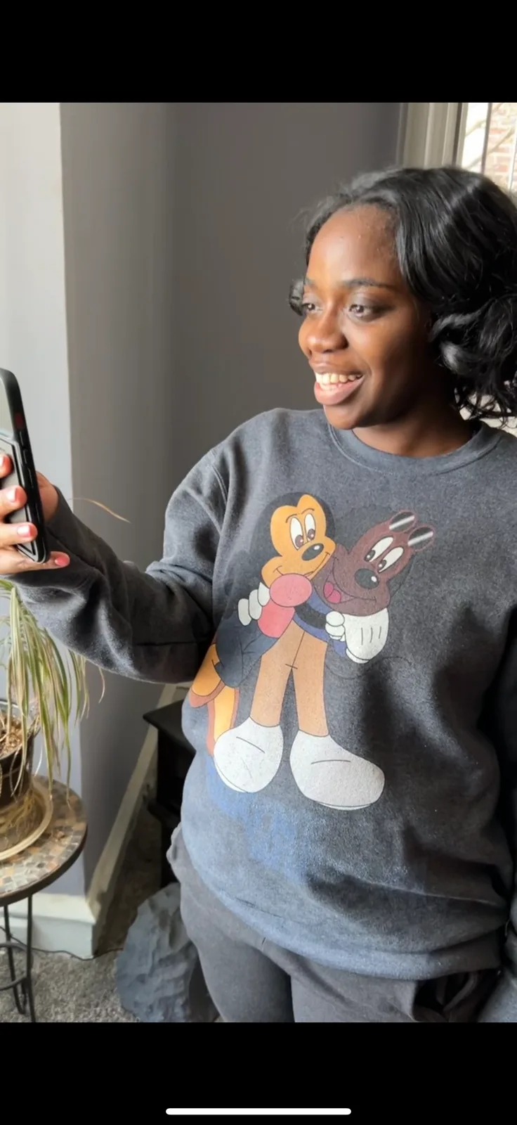 A smiling woman in a Neemo sweatshirt recording herself on her phone to share a story