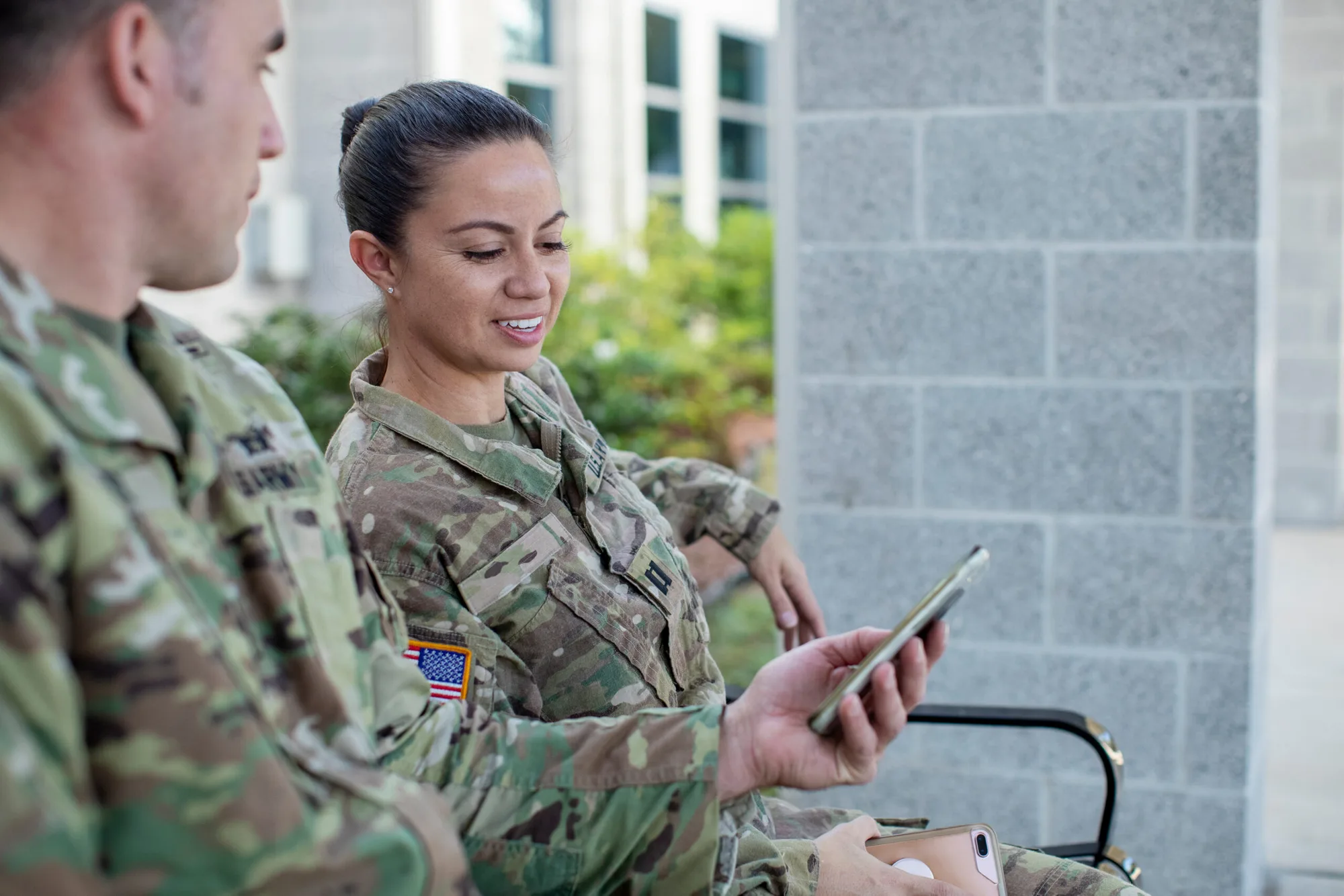 A smiling female soldier watching a video on her phone beside a fellow service member